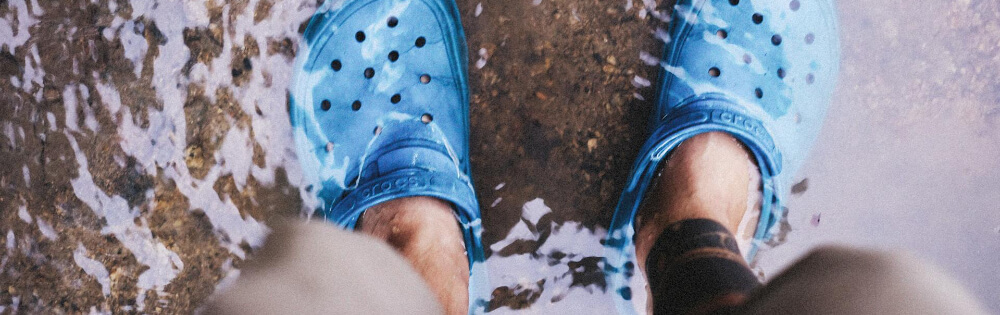 Person steht in kncheltiefem Wasser und trgt blaue Clogs.
